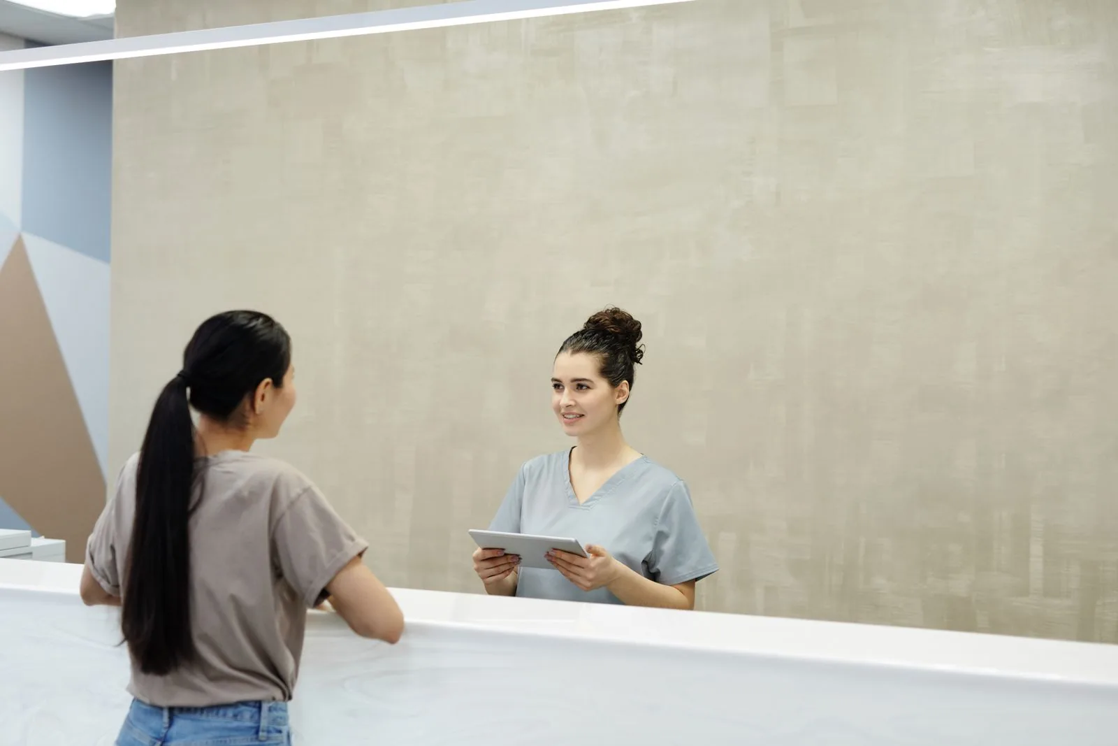 Una receptionist sorridente con un tablet assiste un paziente presso la reception di una struttura medica.