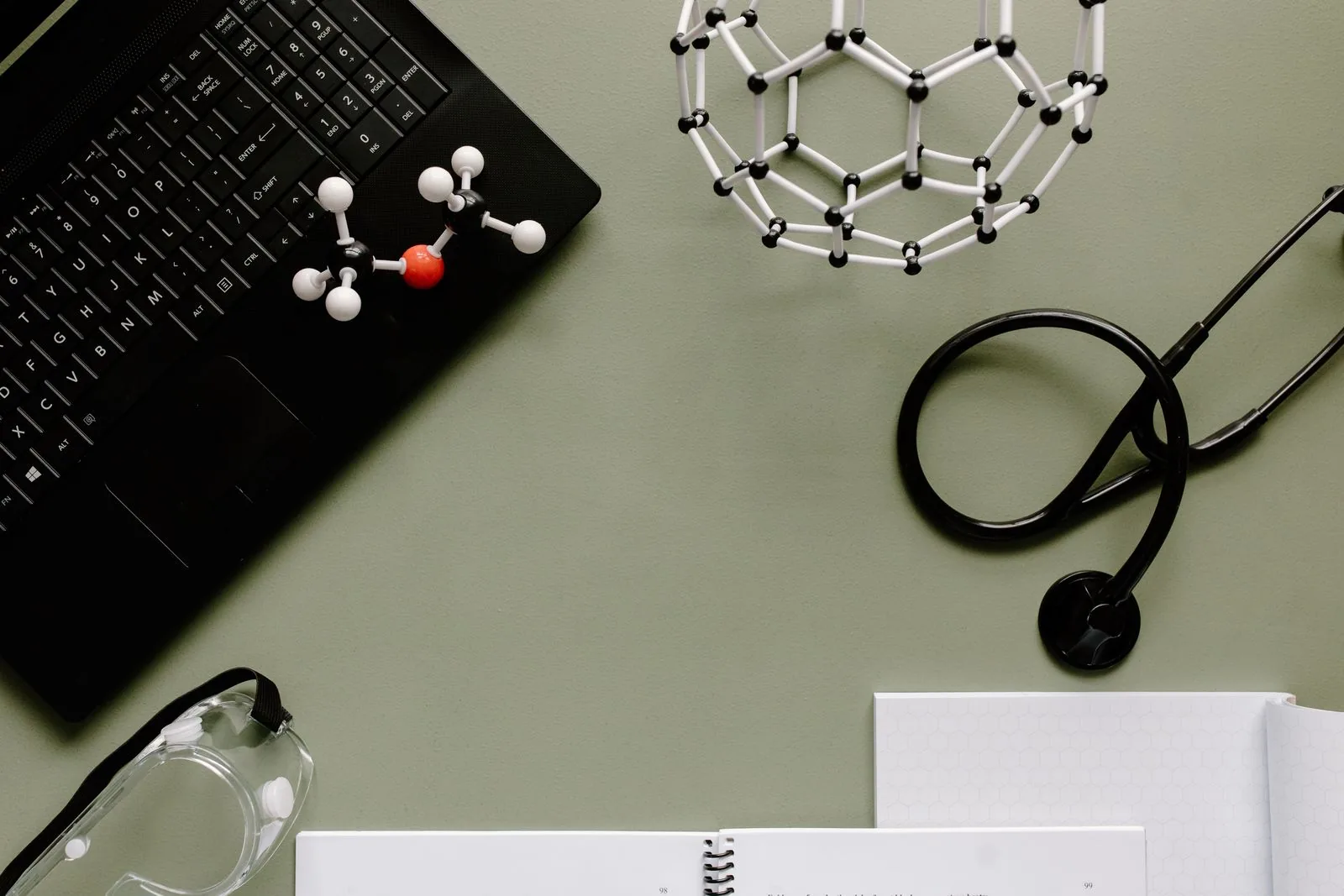 Spazio di lavoro medico con laptop, molecole e stetoscopio su sfondo verde.